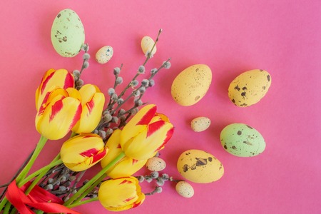 Easter eggs willow branches and yellow tulips on a pink background