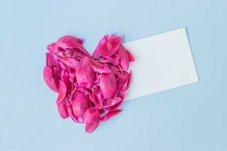 Mockup white greeting card with heart of pink petals on a light blue backgroundの写真素材