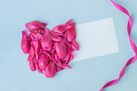 Mockup white greeting card with heart of pink petals on a light blue backgroundの写真素材