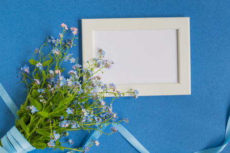 Mockup with a white frame and blue flowers on a blue backgroundの写真素材