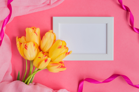 Mockup with a white frame and yellow tulips on a pink backgroundの写真素材