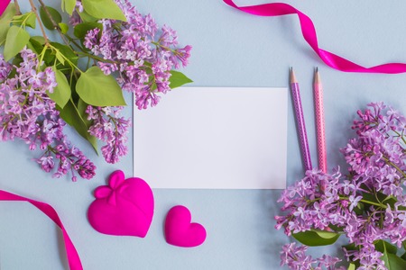 Mockup white greeting card with lilac branches and red ribbon on a light blue backgroundの写真素材