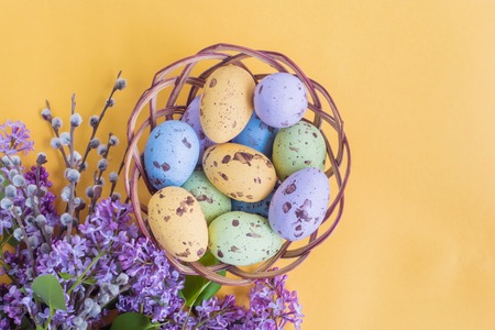 Easter eggs in the basket and lilac branches on a yellow backgroundの写真素材