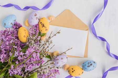 Mockup white greeting card and envelope with lilac branches and easter eggs on a light backgroundの写真素材