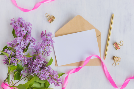 Mockup white greeting card and envelope with lilac branches and pink ribbon on a light backgroundの写真素材