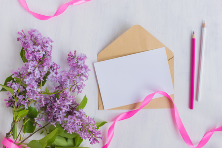 Mockup white greeting card and envelope with lilac branches and pink ribbon on a light backgroundの写真素材