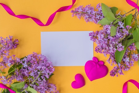 Mockup white greeting card with lilac branches and red ribbon on a yellow backgroundの写真素材
