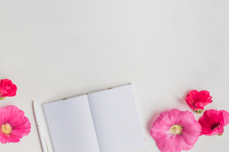 Flat lay desk with pink flowers and notebook on light backgroundの写真素材