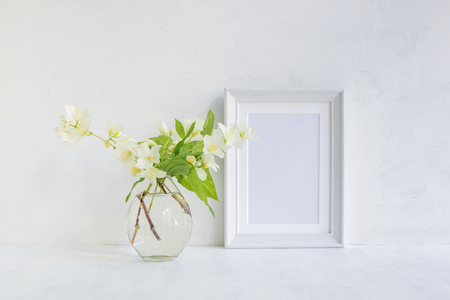 Mockup with a white frame and white jasmine flowers in a vase on a light backgroundの写真素材