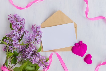 Mockup white greeting card and envelope with lilac branches and pink ribbon on a light backgroundの写真素材