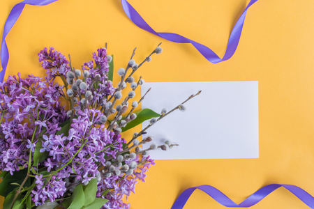 Mockup white greeting card with lilac branches and ribbon on a yellow backgroundの写真素材