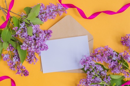 Mockup white greeting card and envelope with lilac branches and pink ribbon on a yellow backgroundの写真素材