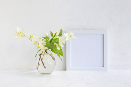 Mockup with a white frame and white jasmine flowers in a vase on a light backgroundの写真素材