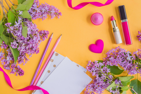 Flat lay desk with lilac branches, notebook and cosmetic on yellow backgroundの写真素材