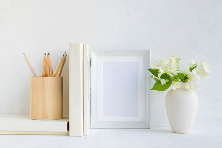 Home interior with decor elements. White frame, flowers in a vase, books and pencilsの写真素材