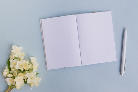 Mockup notebook with white jasmine flowers and light blue background  empty space for your text, top viewの写真素材