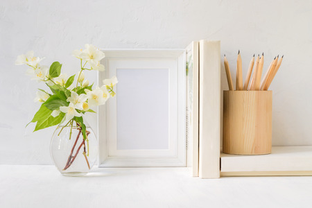 Home interior with decor elements. White frame, flowers in a vase, books and pencilsの写真素材
