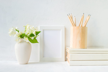 Home interior with decor elements. White frame, flowers in a vase, books and pencilsの写真素材