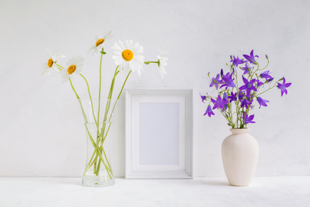 Mockup with a white frame and summer flowers in a vase on a light backgroundの写真素材