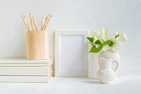 Home interior with decor elements. White frame, flowers in a vase, books and pencilsの写真素材