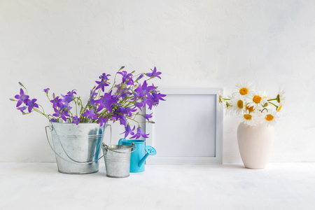 Mockup with a white frame and summer flowers in a metal bucket on a light backgroundの写真素材