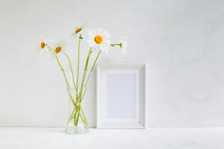 Mockup with a white frame and white daisies in a vase on a light backgroundの写真素材