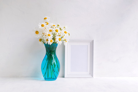 Mockup with a white frame and white daisies in a vase on a light backgroundの写真素材