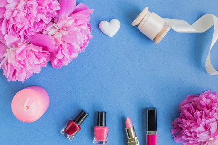 Flat lay desk with pink peonies, cosmetics and accessories on blue backgroundの写真素材