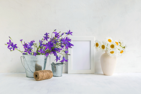 Mockup with a white frame and summer flowers in a metal bucket on a light backgroundの写真素材