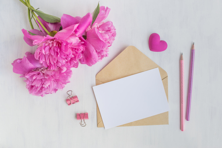 Mockup white greeting card and envelope with pink peonies on a light backgroundの写真素材