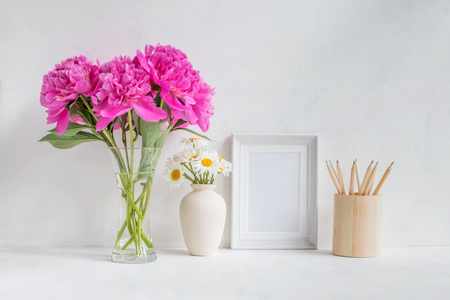 Mockup with a white frame and pink peonies in a vase on a light backgroundの写真素材