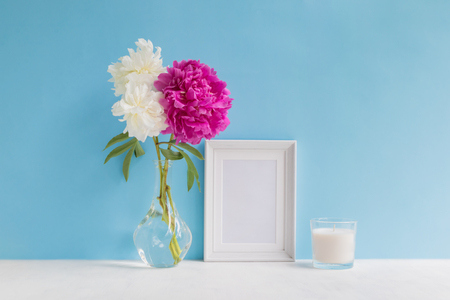 Mockup with a white frame and white and pink peonies in a vase on a blue backgroundの写真素材