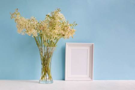 Mockup with a white frame and summer flowers in a vase on a blue backgroundの写真素材