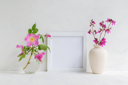 Mockup with a white frame and pink rose hips flowers in a vase on a light backgroundの写真素材