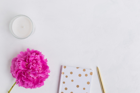 Flat lay desk with pink peony, notebook and accessories on light backgroundの写真素材