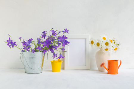 Mockup with a white frame and summer flowers in a metal bucket on a light backgroundの写真素材