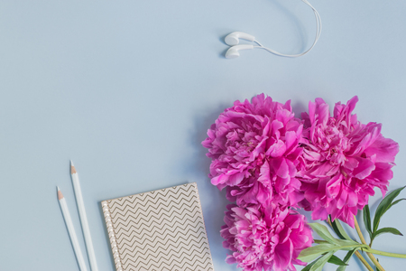 Flat lay desk with pink peonies, notebook and accessories on light blue backgroundの写真素材