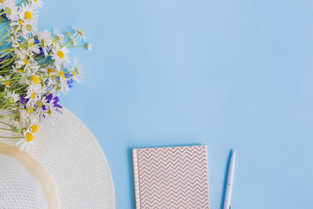 Flat lay desk with summer hat, flowers and notebook on blue backgroundの写真素材