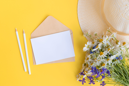 Mockup white greeting card and envelope with summer hat and flowers on a yellow backgroundの写真素材