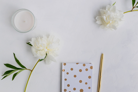 Flat lay desk with white peonies, notebook and accessories on light backgroundの写真素材