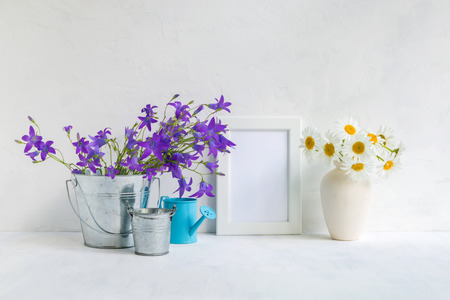 Mockup with a white frame and summer flowers in a metal bucket on a light backgroundの写真素材