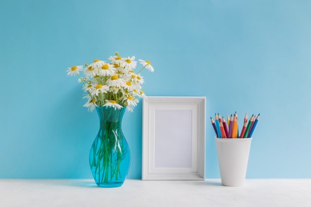 Mockup with a white frame and white daisies in a vase on a blue backgroundの写真素材