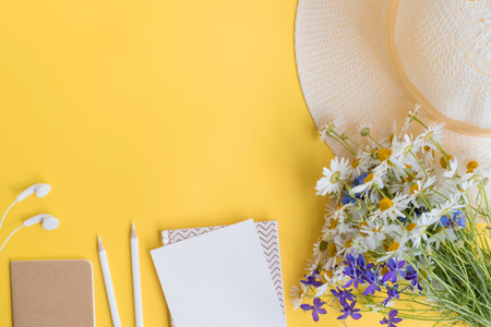 Flat lay desk with summer hat, flowers and notebook on yellow backgroundの写真素材