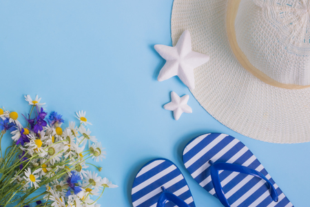 Summer hat, flowers and flip flops on a blue background. Top view, flat layの写真素材
