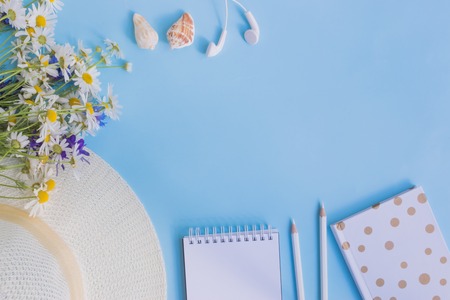 Flat lay desk with summer hat, flowers and notebook on blue backgroundの写真素材