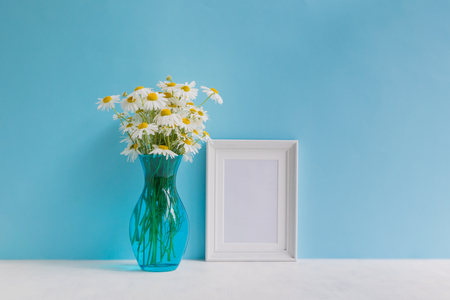 Mockup with a white frame and white daisies in a vase on a blue backgroundの写真素材