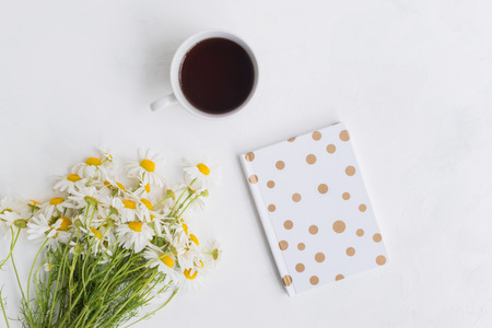 Flat lay desk with white daisies, notebook and cup with tea on light backgroundの写真素材