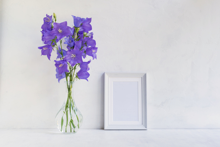 Mockup with a white frame and summer blue flowers in a vase on a light backgroundの写真素材