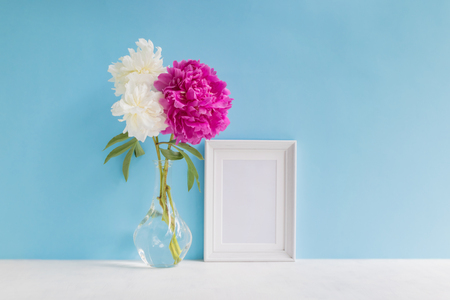 Mockup with a white frame and white and pink peonies in a vase on a blue backgroundの写真素材