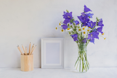 Mockup with a white frame and summer blue flowers in a vase on a light backgroundの写真素材